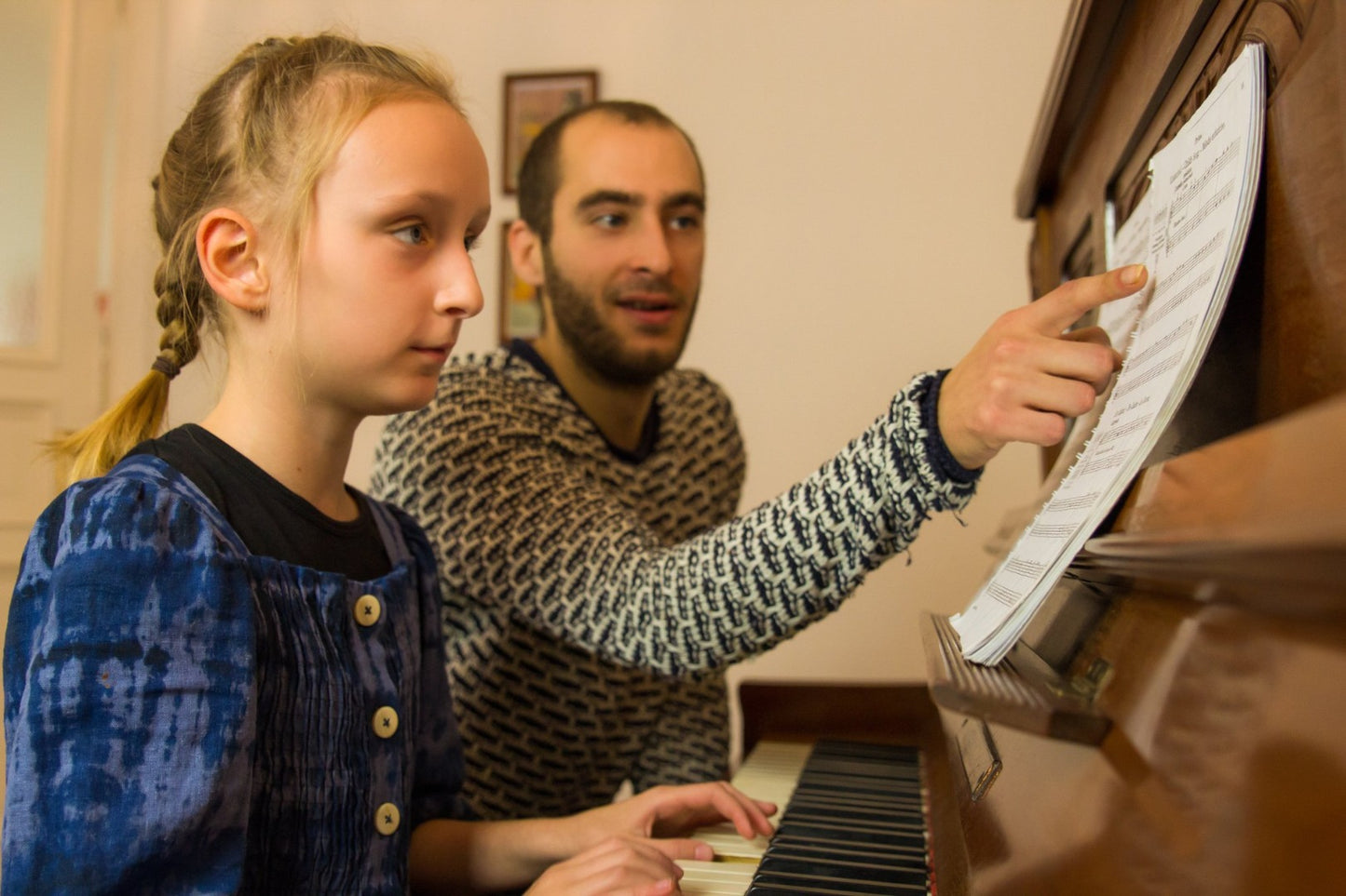 Junges Mädchen beim Klavierunterricht. Ihr Lehrer zeigt ihr die Noten. Sie sitzen an einem richtigen Klavier.