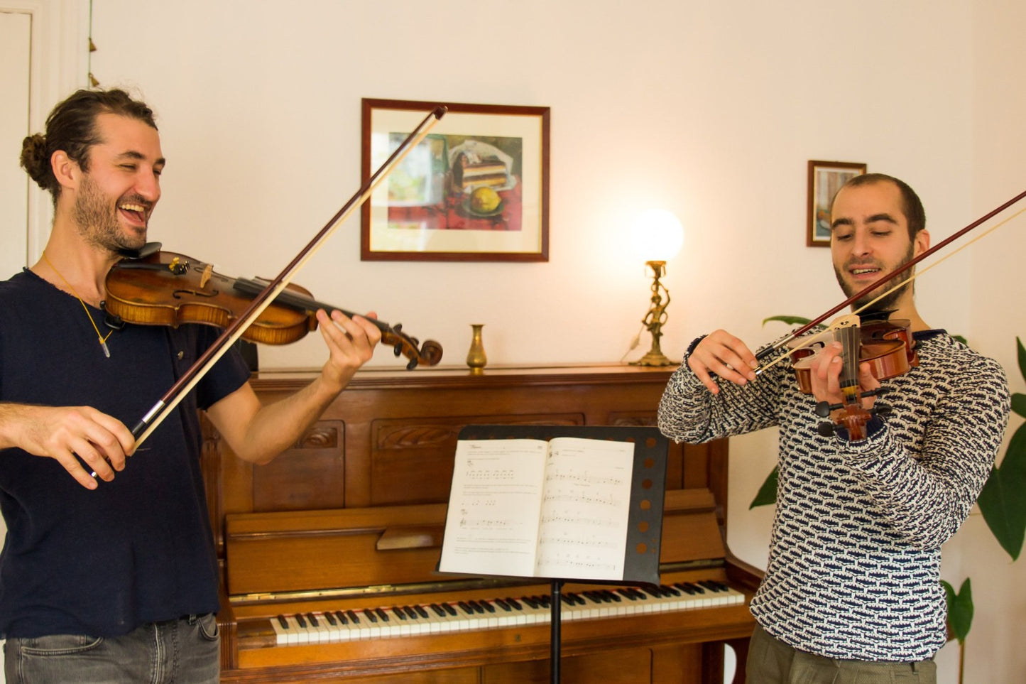 Auf diesem Bild sind zwei junge Männer mit Violinen zu sehen. Sie haben viel Spaß beim Geigenunterricht.